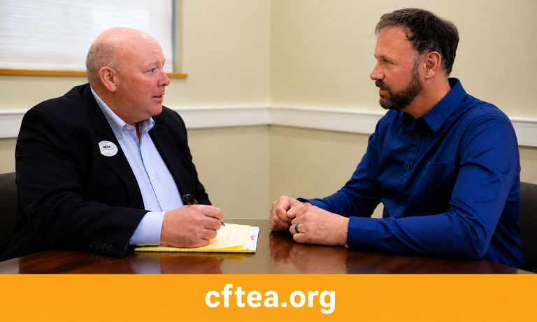 Wide banner showing two professionals seated across from each other at a conference table during a one-on-one conversation. On the left, a man in a dark blazer holds a pen over a notepad as he listens attentively. On the right, Andrew, wearing a royal blue button-down shirt, leans forward with his hands folded, maintaining focused eye contact. Their expressions convey active listening, mutual respect, and thoughtful discussion in a professional meeting setting. A gold bar spans the bottom of the image with "cftea.org" centered in white text. The image emphasizes the value of meaningful conversations, coaching, and professional relationships.